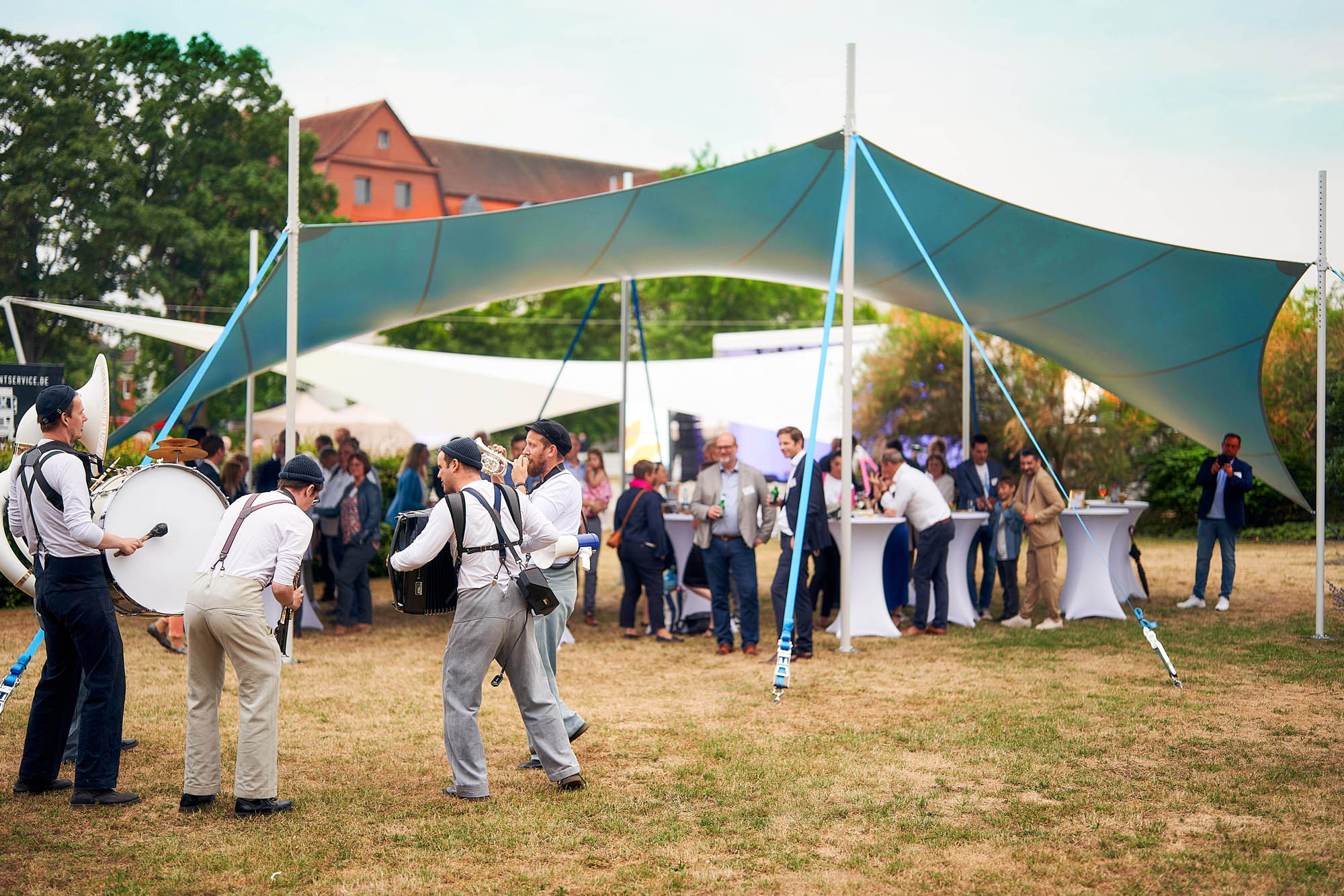 Ein schickes türkisfarbenes Sonnensegel während eines Sommerfests mit Livemusikern und Gästen.